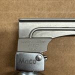Close-up of a metal lighter head with engraved text: 'Welch Allyn 69472 Mac' on a silver latch, against a brown background.
