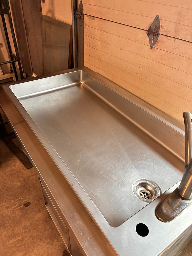 Large stainless steel utility sink in a garage/workshop with a high faucet and round drain drain visible in the basin edge.