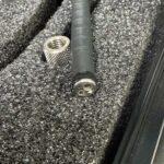 Close-up of a black cable with a three-pin round connector on the end, resting in foam alongside a knurled metal connector.