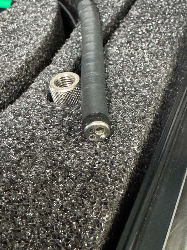 Close-up of a black cable with a three-pin round connector on the end, resting in foam alongside a knurled metal connector.